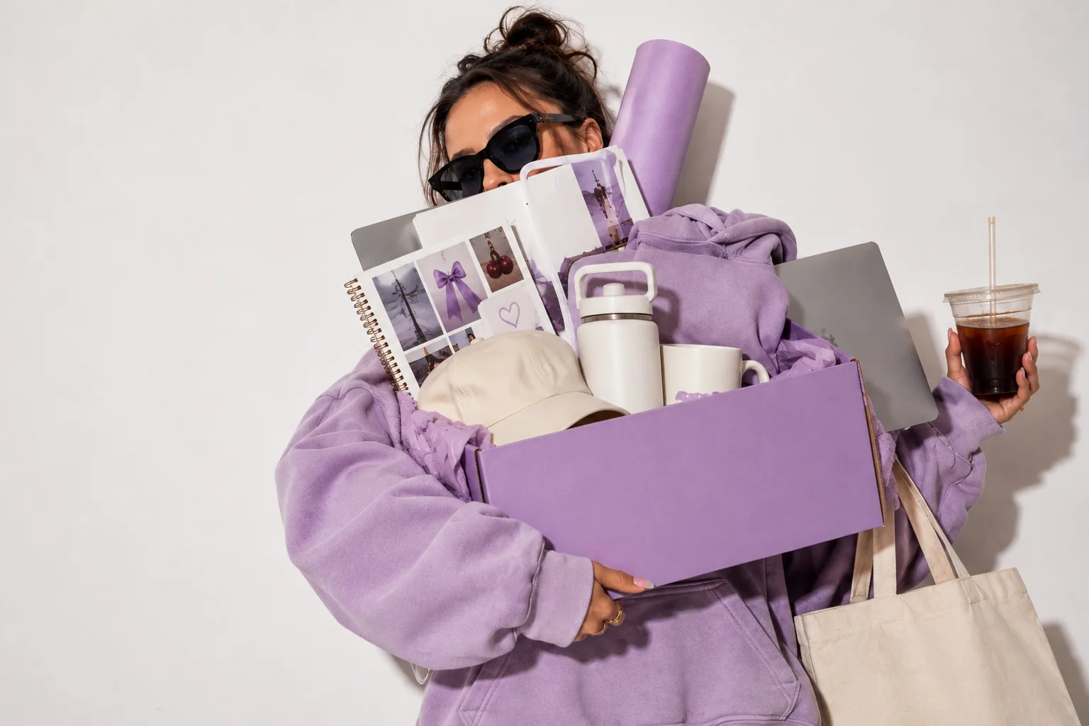 Someone carrying a lavender box full of their own branded hoodie, mug, hat, tote and notebook